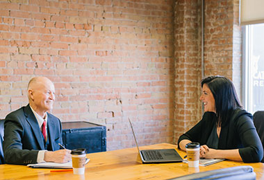 business man and woman smiling and sitting at a conference table
