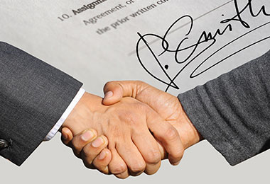 two men shaking hands over signed document