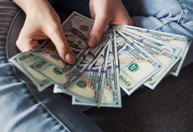 lady fanning out a small stack of hundred-dollar bills