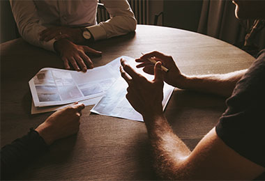 three people sitting at a round table reviewing paperwork