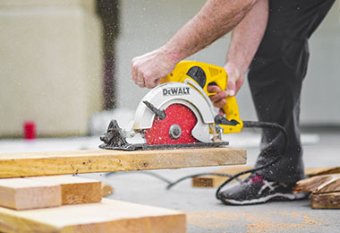 man cutting boards with a circular saw close to his foot